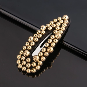 Detail of a black teardrop hair clip with elegant gold beaded studs on dark background