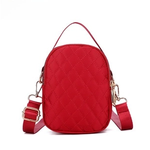 Detail of red quilted crossbody bag with golden metal zipper and adjustable strap