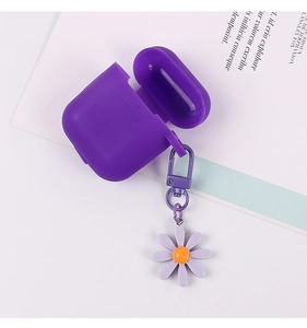 Purple silicone AirPods case with a cute daisy flower metal pendant on a book background