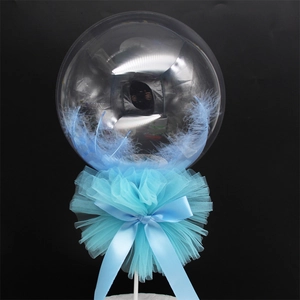 Detailed view of clear cake balloon with blue feathers and decorative mesh bow on a stand