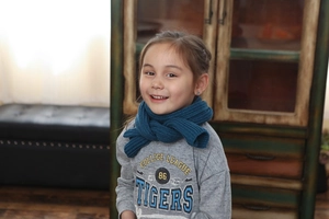 Detail shot of a dark blue ribbed knit winter scarf styled on a child in a home setting