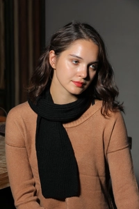 Detail shot of black knitted scarf with vertical rib pattern worn over a camel sweater