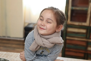 Detail shot of a young girl wearing a cozy beige knitted scarf in a warm indoor setting