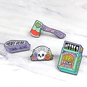 Flat lay of colorful skull, coffin, and matchbox enamel pins on marble background