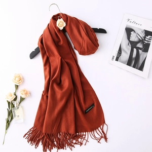 Close-up of orange cashmere scarf fabric with elegant tassels and stitched gold label