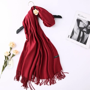 Detail of red cashmere scarf with tassels hanging naturally next to a rose and perfume