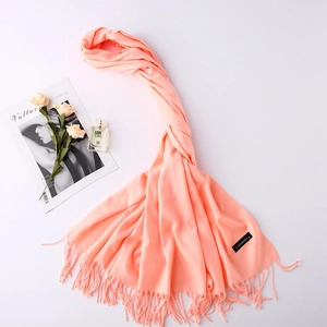 Flat lay of pink-orange cashmere scarf with fringes, flowers, and magazine decor
