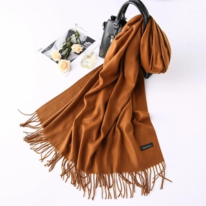 Detail of caramel cashmere wool scarf with soft fringed edges and brand label on white
