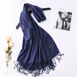 Detail of dark blue cashmere scarf with dense tassels and material label on wooden hanger