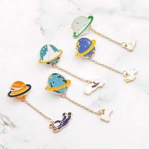 Five planet and astronaut enamel brooches with gold chains on marble background