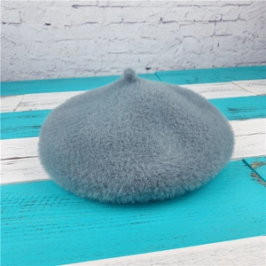 Plush grey-blue faux rabbit fur beret with fluffy texture on blue-white wooden background