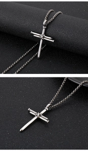 Macro detail of silver nail cross pendant on black textured background with metal chain