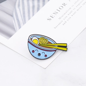 Close-up of a cute blue enamel ramen bowl pin with yellow noodles and eggs on a table