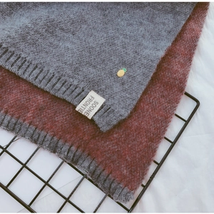 Gros plan d'écharpes tricotées gris et bordeaux avec broche ananas sur support grillagé