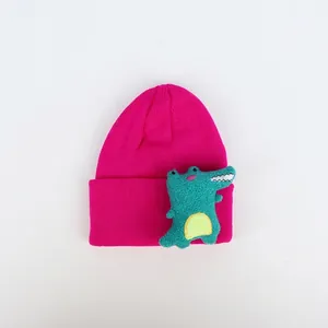 Detailaufnahme einer pinkfarbenen Strickmütze mit 3D-Dino-Puppe am umgeschlagenen Rand