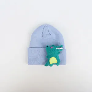 Detail einer hellblauen Strickmütze mit strukturiertem 3D-Dinosaurier-Patch in Grün