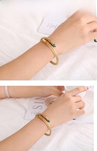 Detail of gold cable twist cuff bracelet with green stone tips on white linen cloth