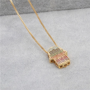 Macro detail of golden Hamsa hand pendant with colorful zircons on gray velvet