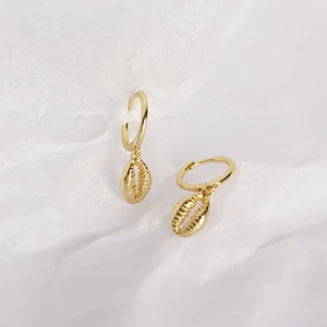 Macro shot of gold shell pendants on s925 silver hoop earrings on white paper background