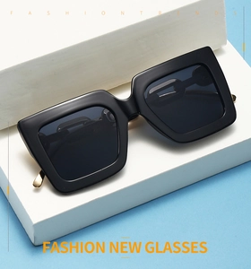 Détail de lunettes de soleil carrées noires avec charnière en métal doré sur socle blanc