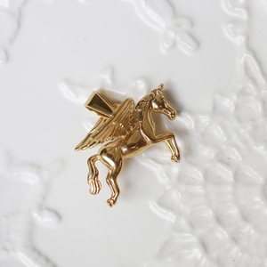 Macro shot of 18K gold plated Pegasus pendant with detailed wings on white surface