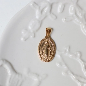 Macro shot of 18K gold religious Virgin Mary oval medallion pendant on white ceramic plate