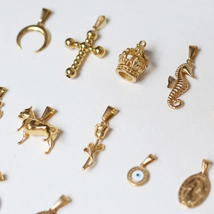 Detail shot of assorted 18K gold plated titanium steel charms on a white surface