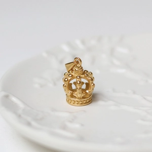 Detailed close-up of a 18K gold crown pendant on a white embossed decorative plate