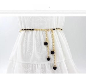 Detail view of a gold chain belt with black woven cord and elegant hanging black beads