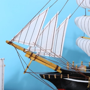 Maquette de voilier classique en bois avec coque noire et voiles blanches sur bleu