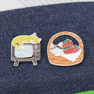 Detail of cartoon enamel pins featuring a cat on a TV and a kitten in a strawberry basket
