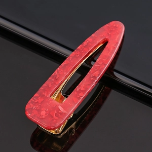 Detail of red marbled acetate hair clip with golden metal base on a black surface