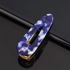 Macro shot of blue marble acetate hair clip with gold metal base on a black background