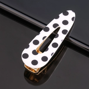 Close-up of a white acetate hair clip with black polka dots and golden metal clip base