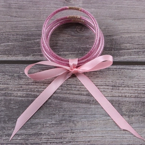 Detail of pink glitter jelly bracelets with ribbon bow on a wooden texture background