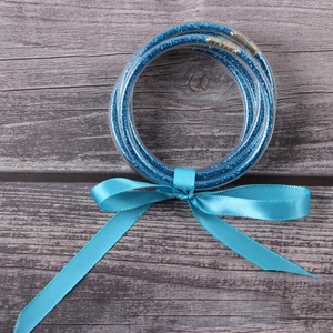 Flat lay of blue glitter jelly bracelets with a matching satin ribbon bow on wood