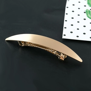 Minimalist gold curved metal hair clip with a polished finish on a dark background