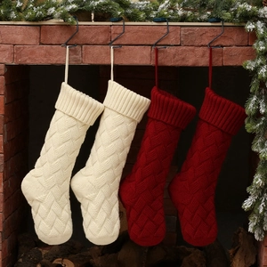 Classic cable knit Christmas stockings in ivory and dark red hung on a rustic fireplace