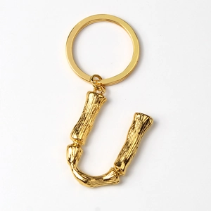 Detailed close-up of golden metal letter U keychain with textured bamboo pattern design