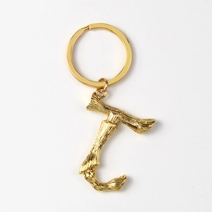 Close-up of golden letter T keychain with realistic bamboo texture and polished metal ring