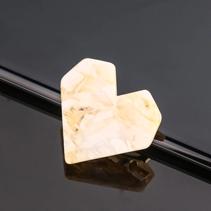 Macro shot of heart-shaped hair clip with beige marble texture and smooth resin finish
