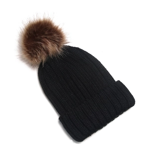 Black winter knit beanie featuring a fluffy brown faux fur pom pom on white background