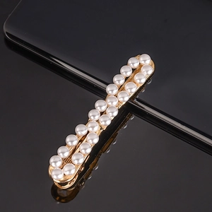 Close-up of golden hair clip with double-row faux pearls on reflective black surface