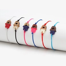 Detailed view of six colorful woven friendship bracelets with house charms on a white stand