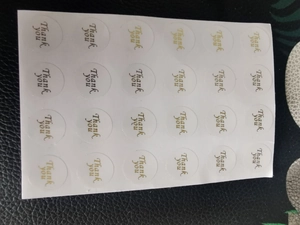 Detail view of round 'Thank You' stickers with black and gold cursive on white backing