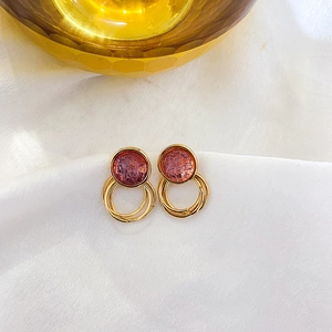 Detail of gold double hoop earrings featuring pink faux gemstone with natural textures