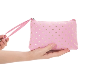 Detail of pink fabric makeup bag with gold dots held by hands to show size and portable handle