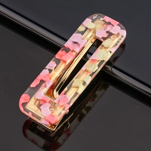 Detailed close-up of a pink acetate resin hair clip with a golden metal base and shell texture