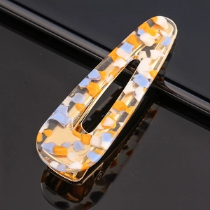 Detail of hollow acetate hair clip with blue and orange stone patterns on gold metal base