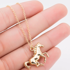 Détail du pendentif cheval doré tenu à la main pour montrer la taille de ce bijou chic